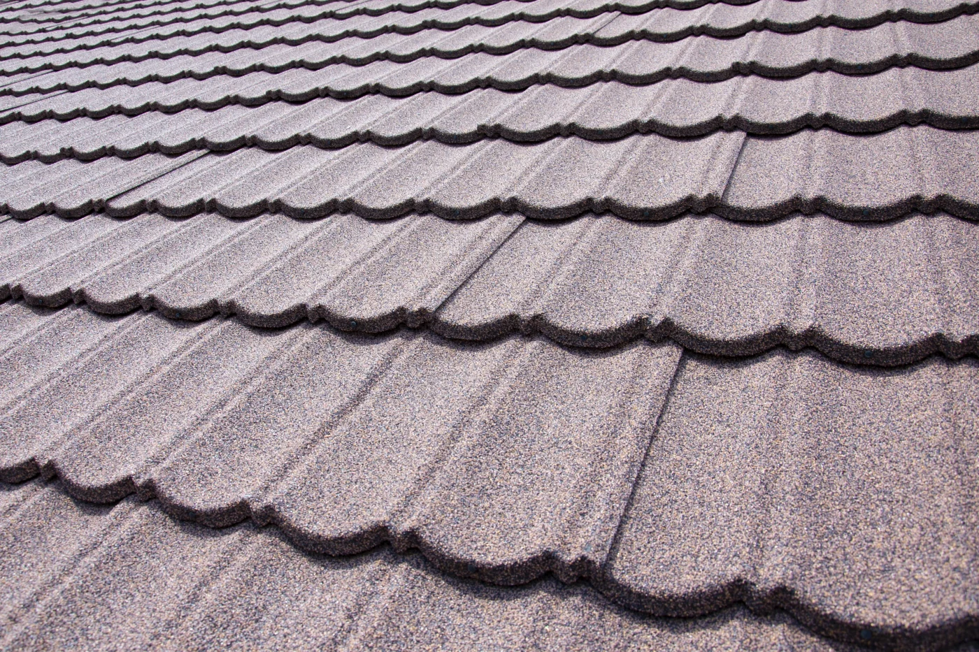 The joint of a rooftop where two sides meet. The roof is covered in a brown, metal material that looks like elongated rectangular shingles.