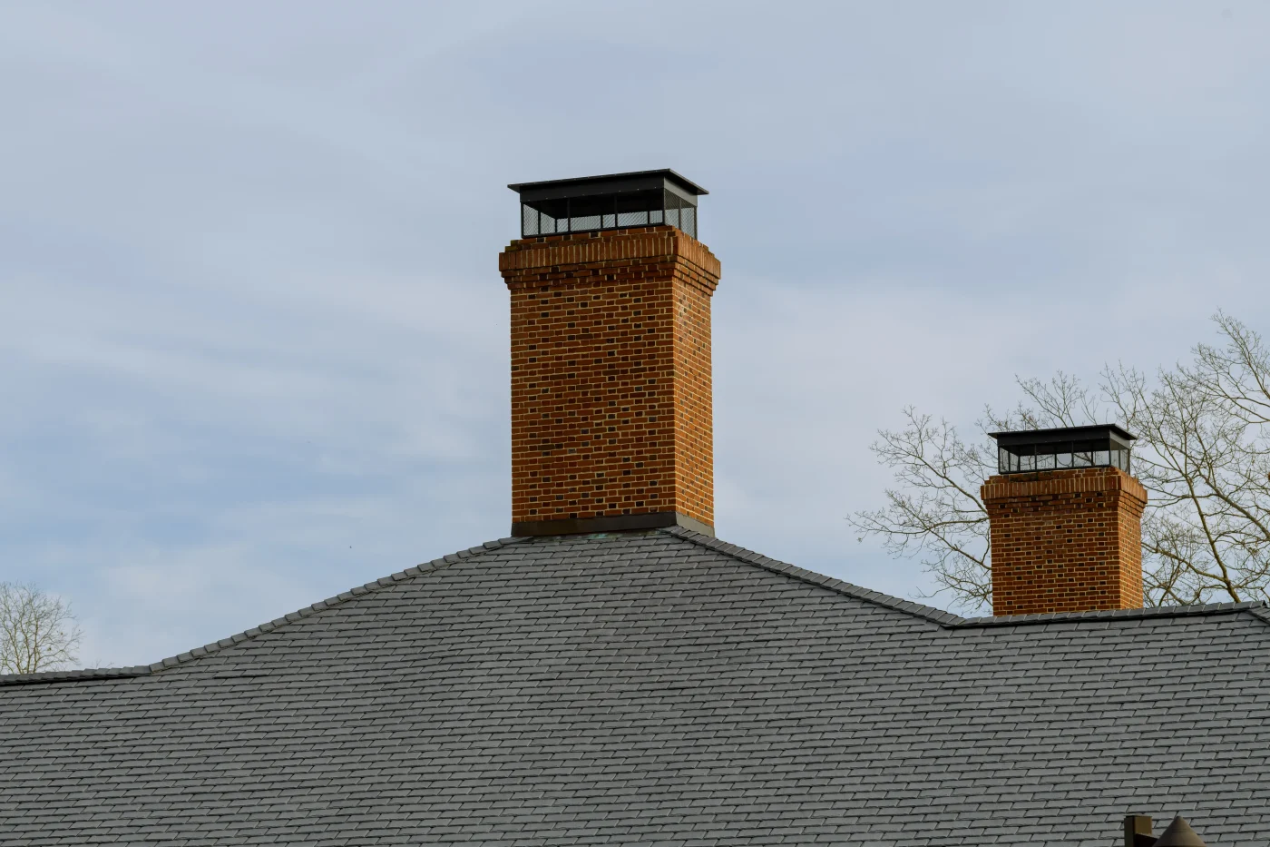 An orangey-red brick chimney on a terra-cotta colored tile roof. There is some snow on the roof, obscuring some of the tiles.