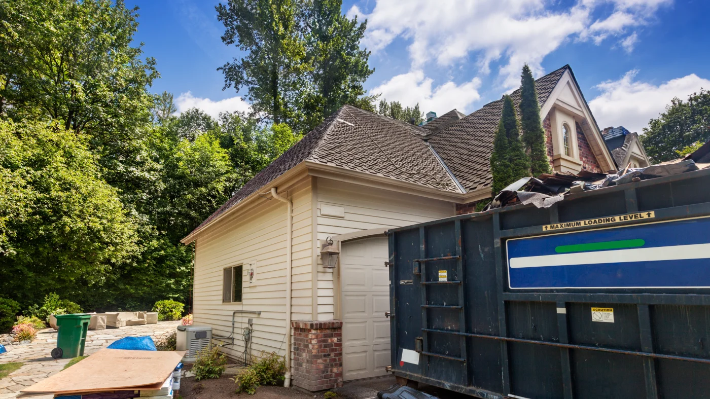 A close view of the dumpster and side yard of a home undergoing a roof replacement.