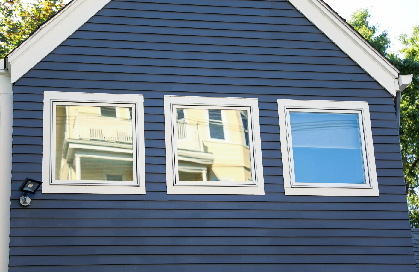 A trio of square windows with white trim. The windows are located on the side of a house covered in dark blue siding.