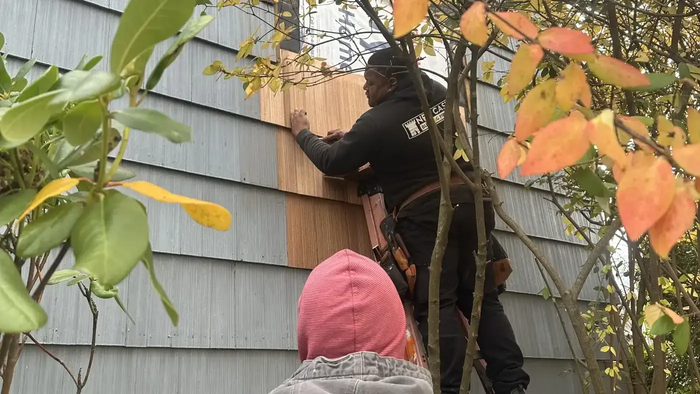 Two Sound Renovation crew members patching damaged cedar siding on a local home.