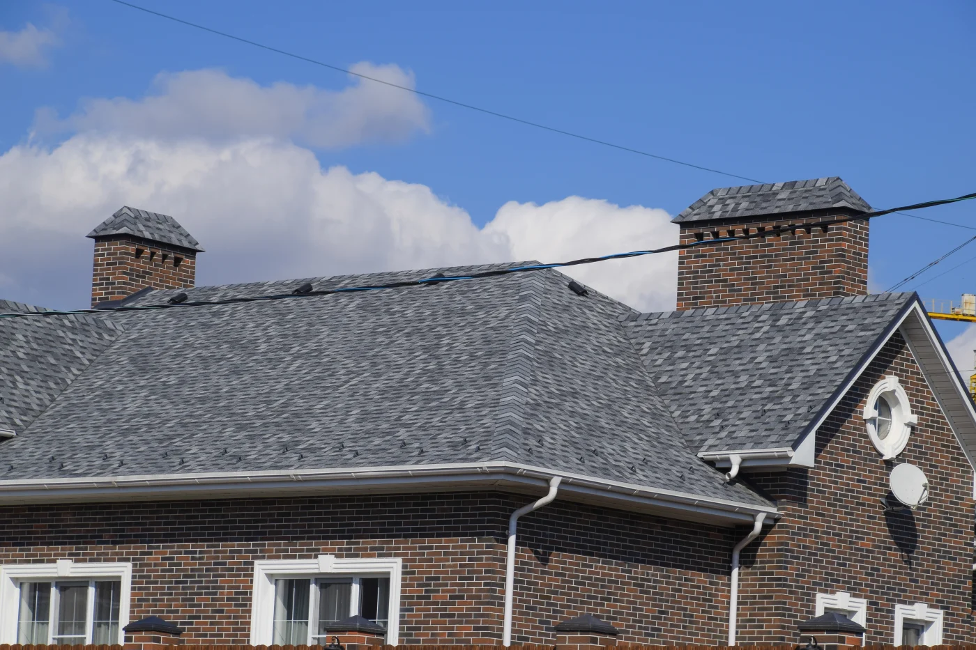 A home with a dark brick exterior and a gray, shingled roof. The home has white gutters and window trim