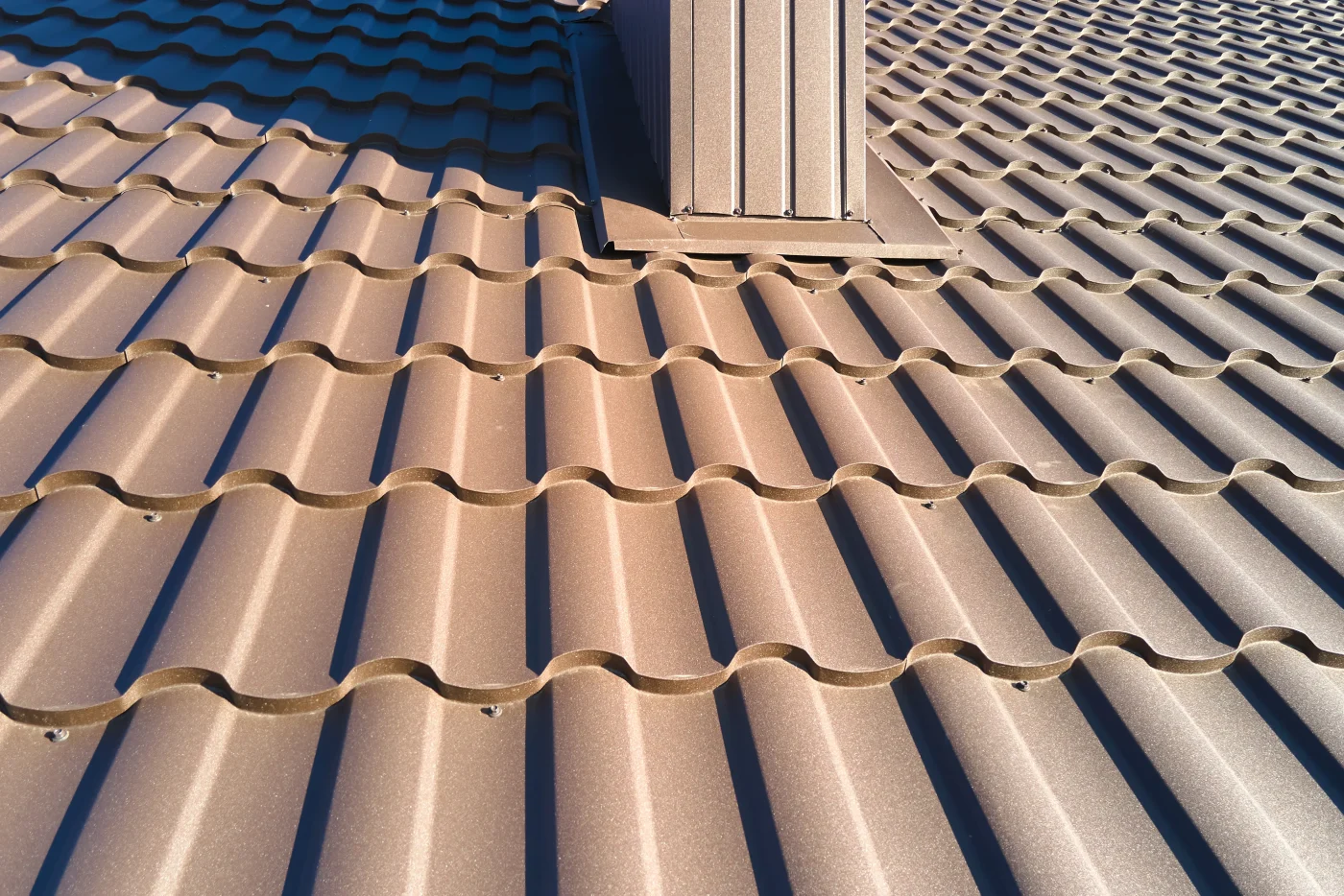 A close-up view of a dark brown rooftop covered in metal roofing material. The tiles have a scalloped edge.