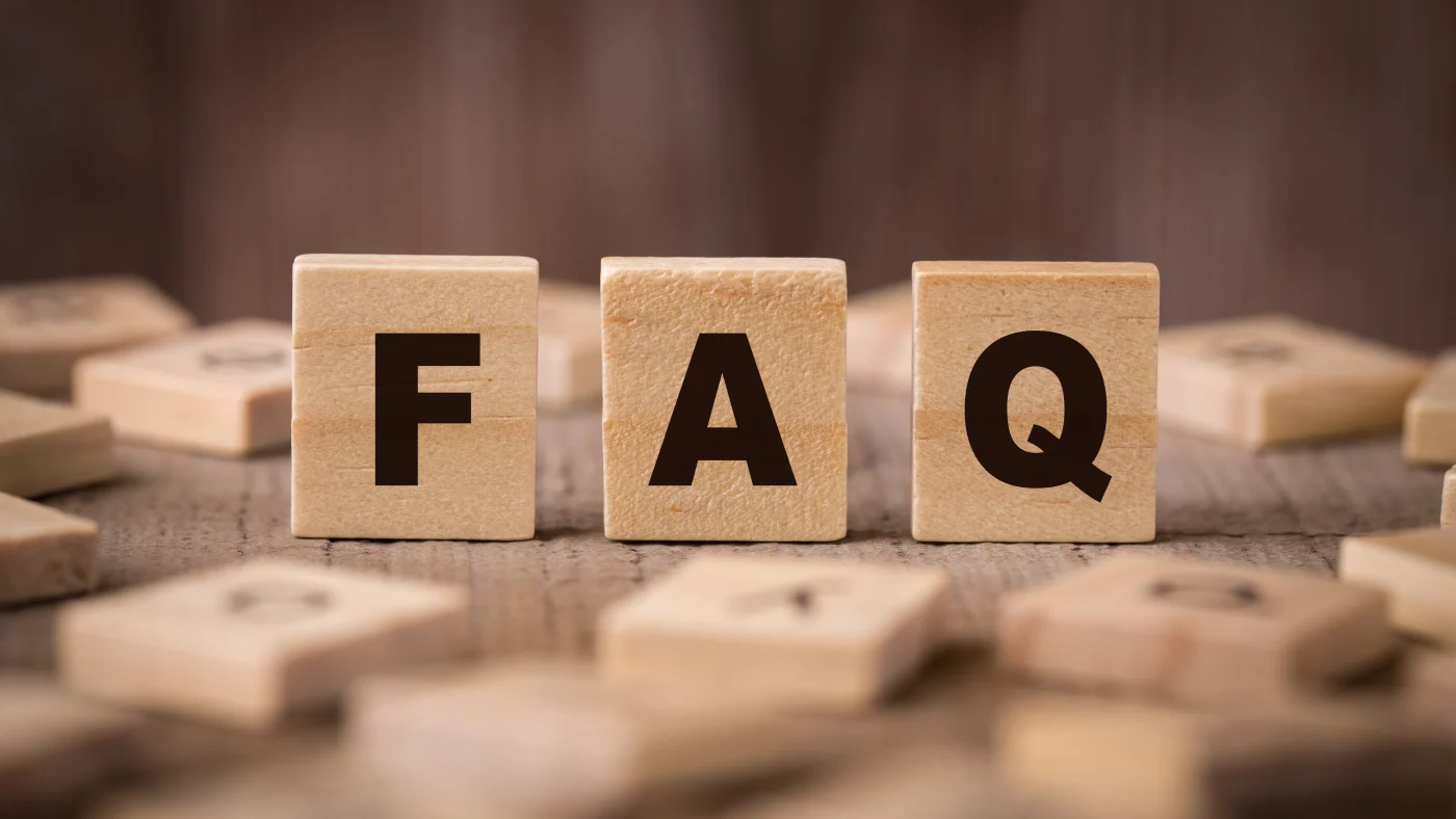 Close-up frontal view of a man sitting at a table, placing the last of three small wooden blocks that spell out “FAQ.”
