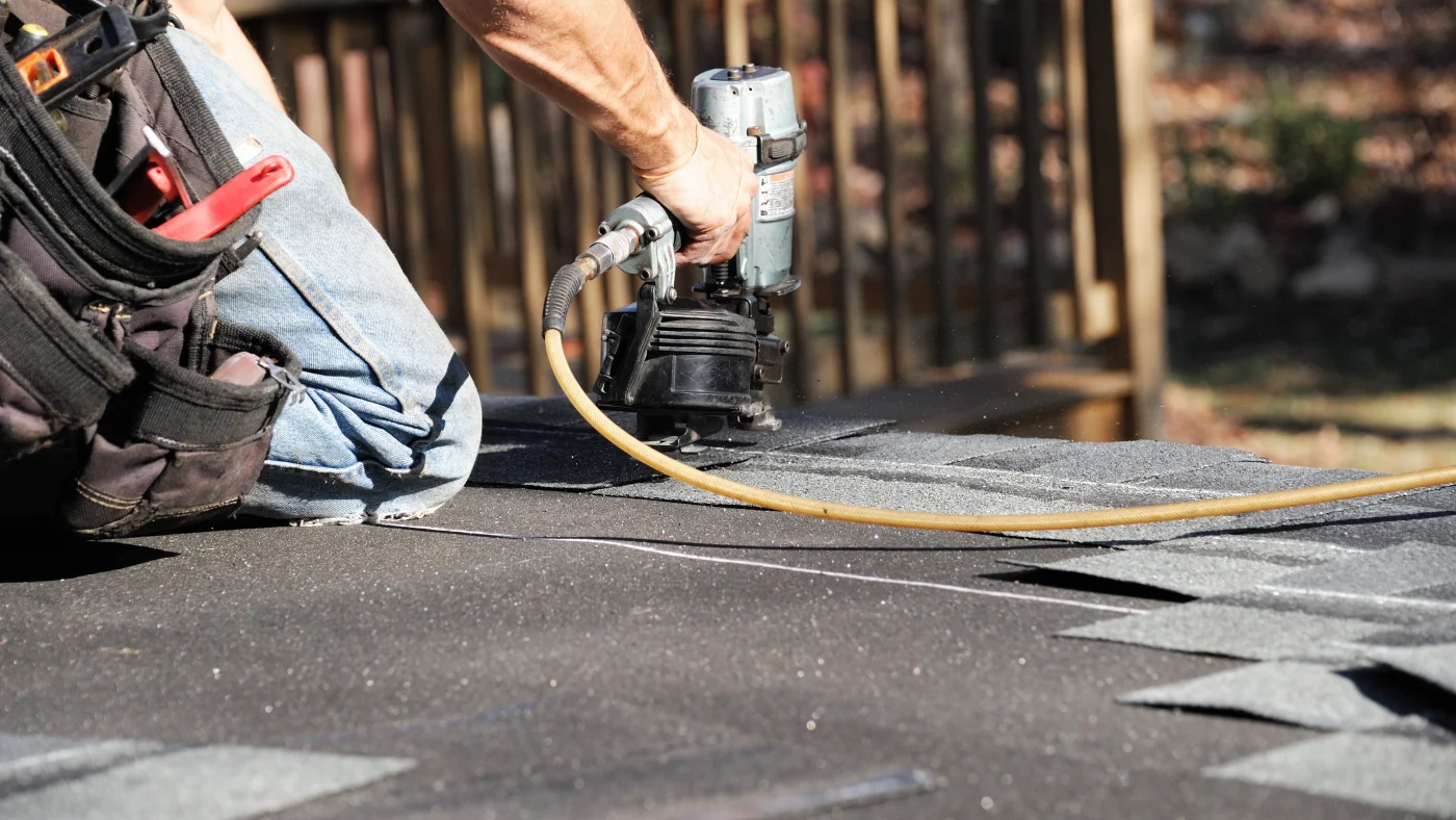 A close view of a roofer with a nailgun making a repair in an asphalt roof.