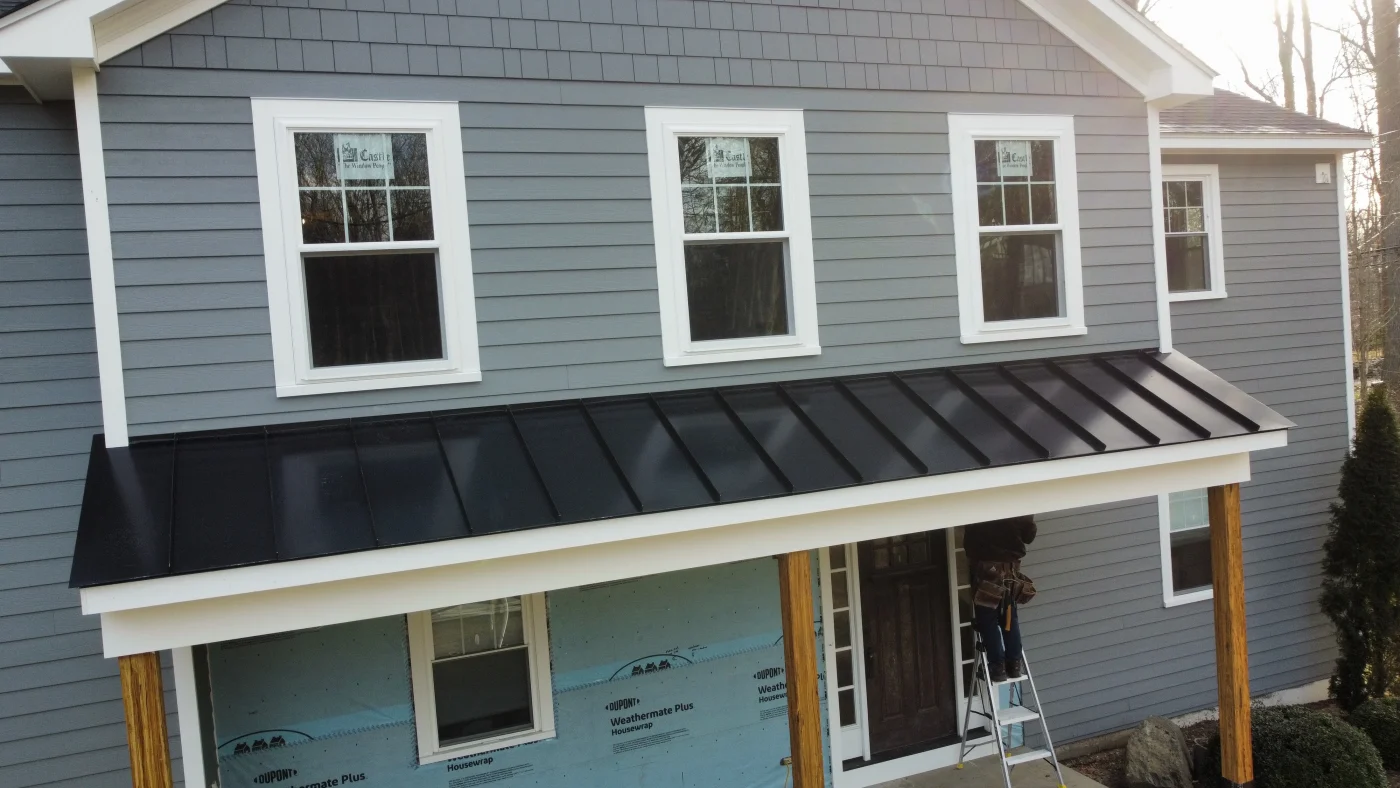 A black standing seam metal roof over a small landing on a two-story home.