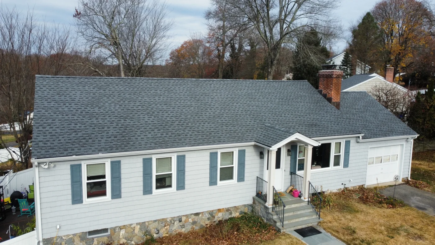 Professional Residential Roof Replacement In Weston, CT | Sound Renovation A newly shingled asphalt roof on a home framed by mature trees on a clear day.
