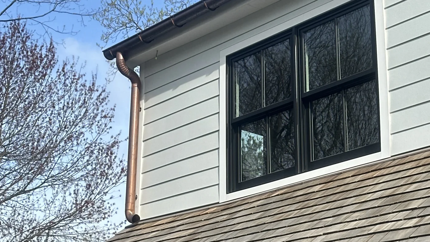 The upper level of a home with yellow siding, white gutters, and trim. The window frames are white, too.