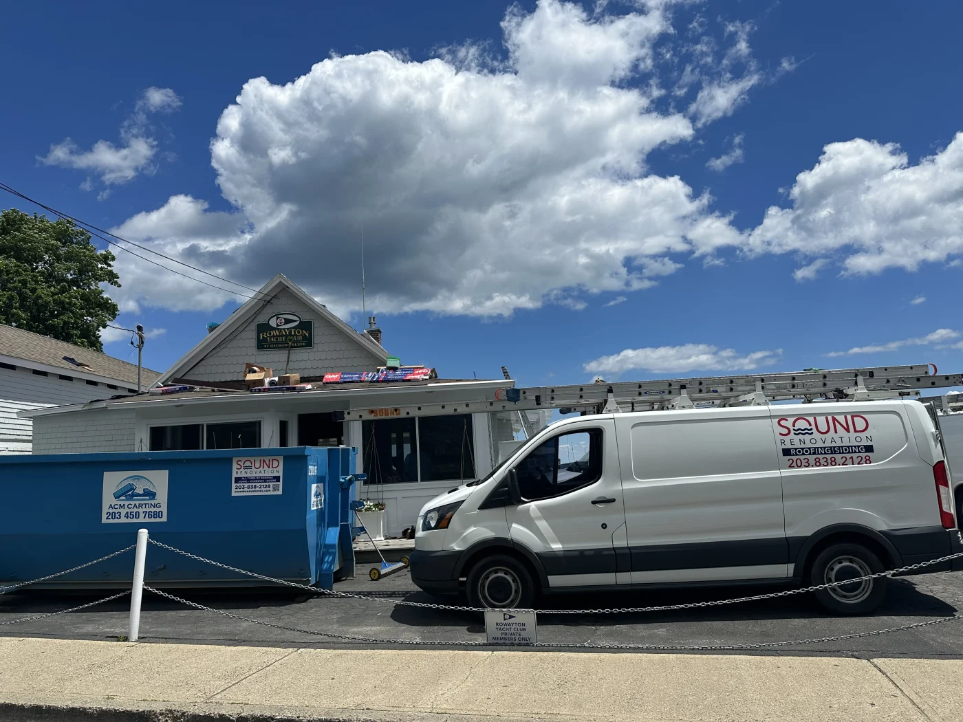 A Sound Renovation company vehicle near a dumpster as roof work takes place on a commercial building.