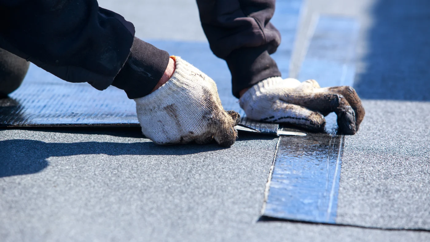 A close view of a roofer’s hands as he performs a repair on an asphalt shingle roof.
