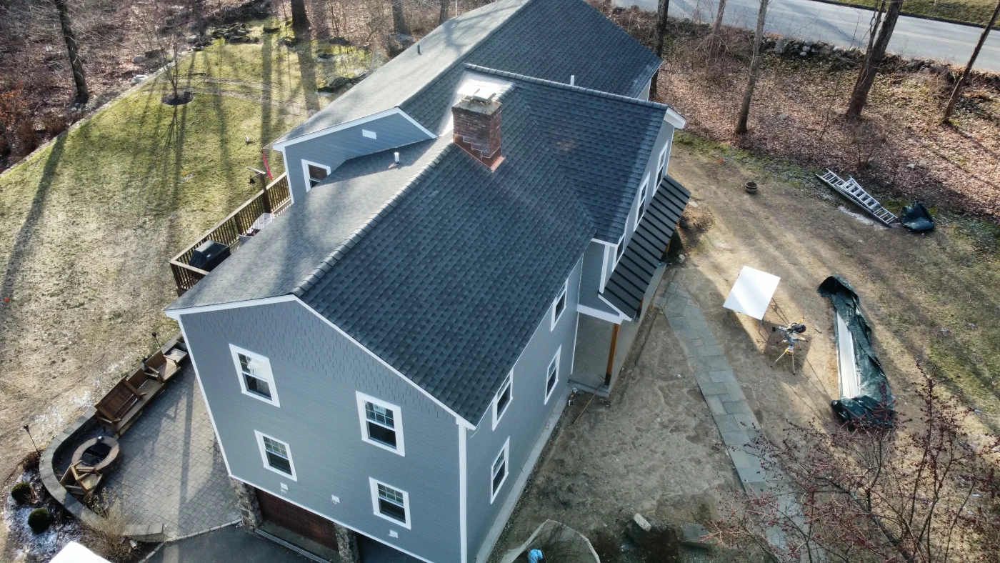 A finished asphalt shingle roof on a two-story colonial home surrounded by mature trees.