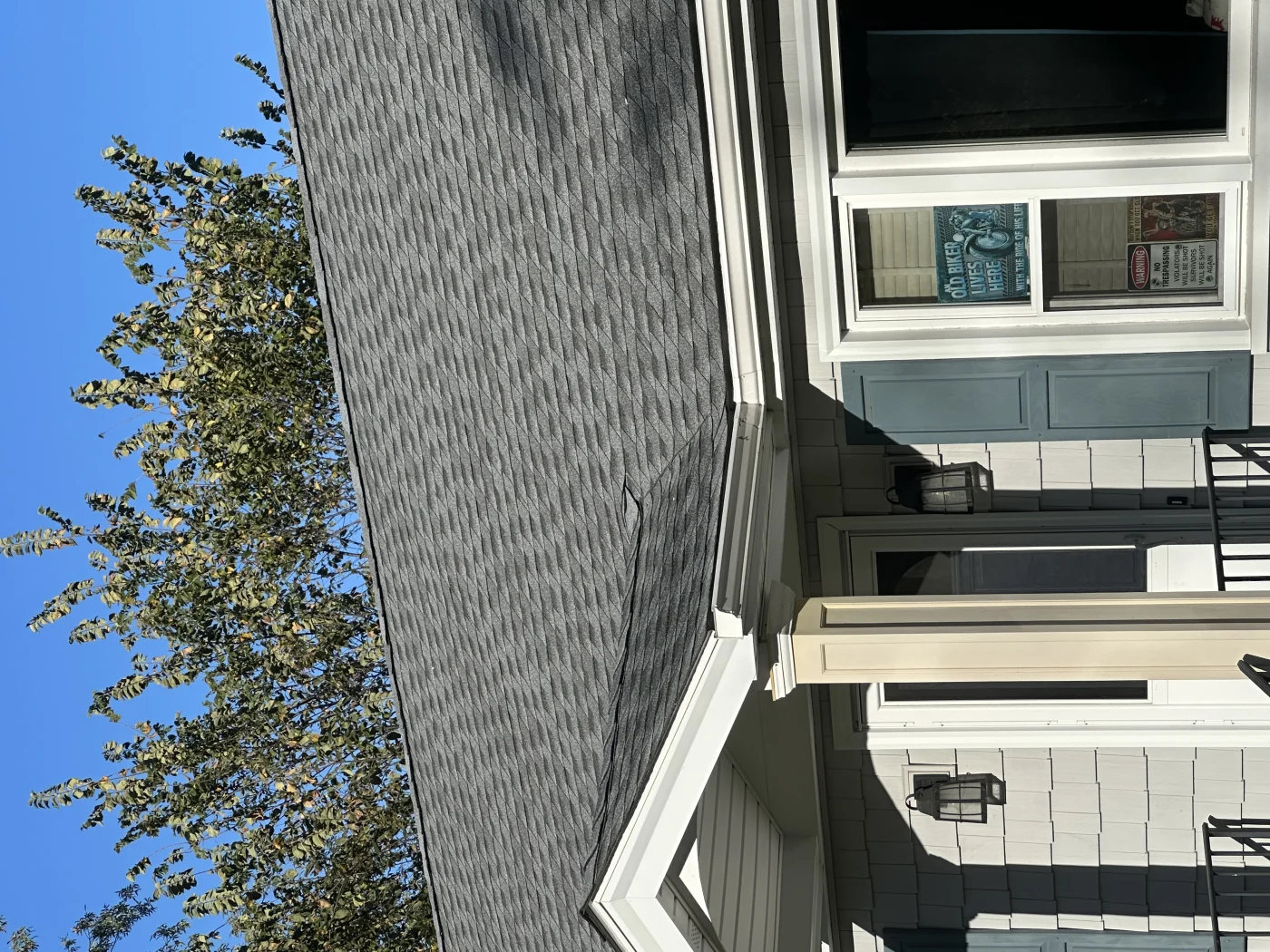 A close-up of the section of a gray shingled roof above a small covered front porch. The home has blue-gray window shutters, white gutters and trim, and a light gray, shingled exterior.