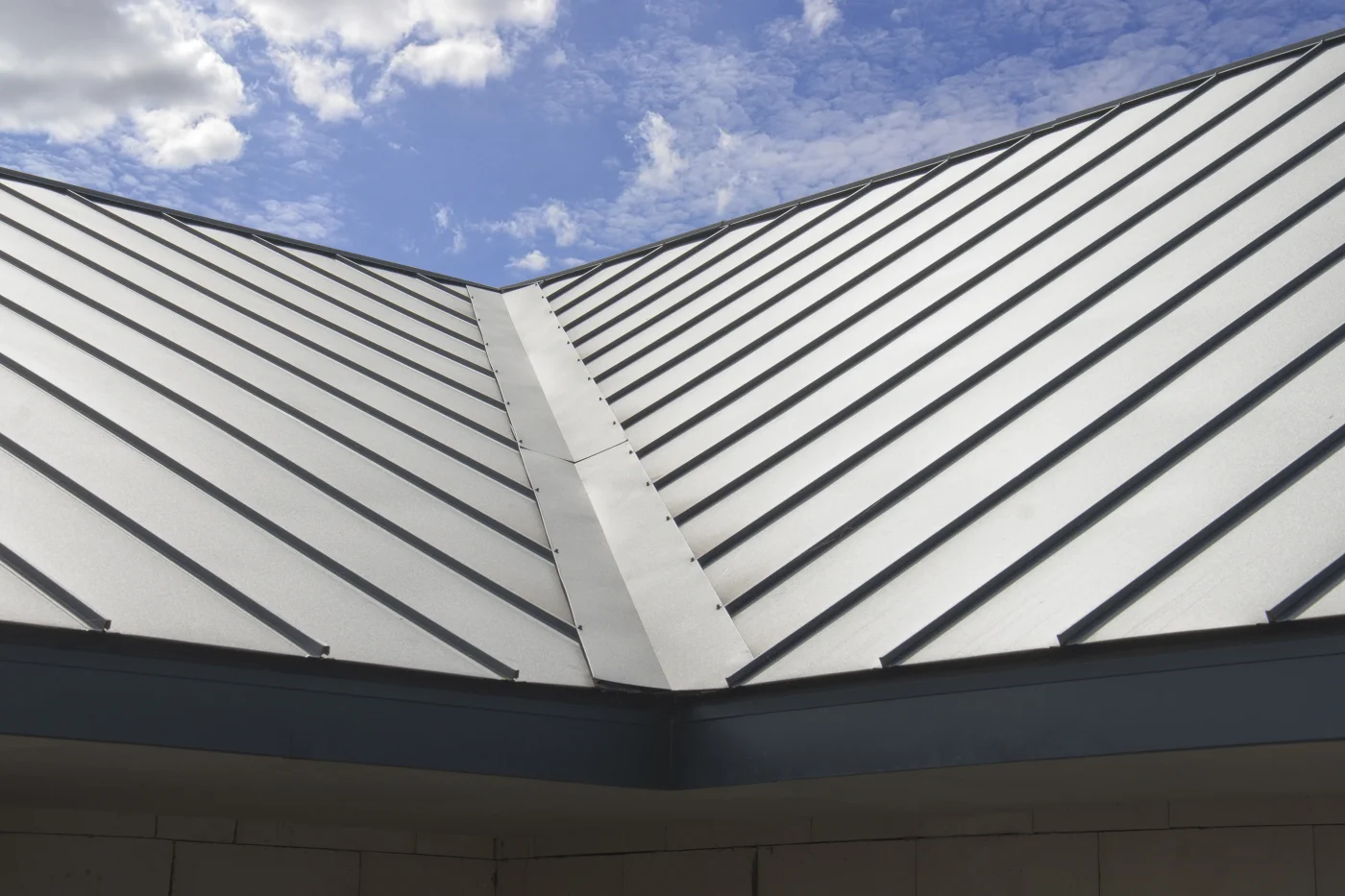 A corner section of a roof covered in black standing seam metal panels. Below the roof, the exterior of the home is white brick.