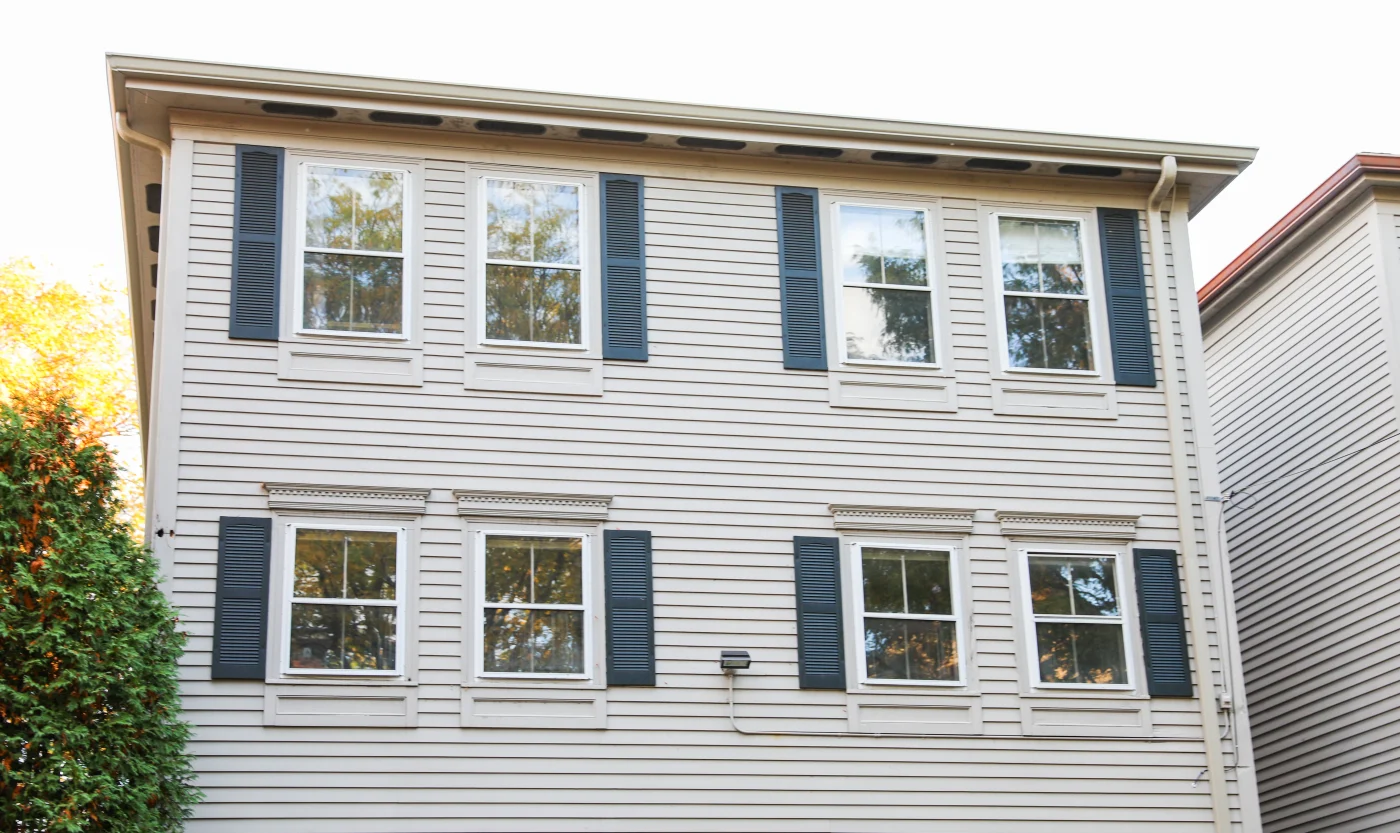 A two-story home with white siding and blue window shutters. There are four visible windows on each floor