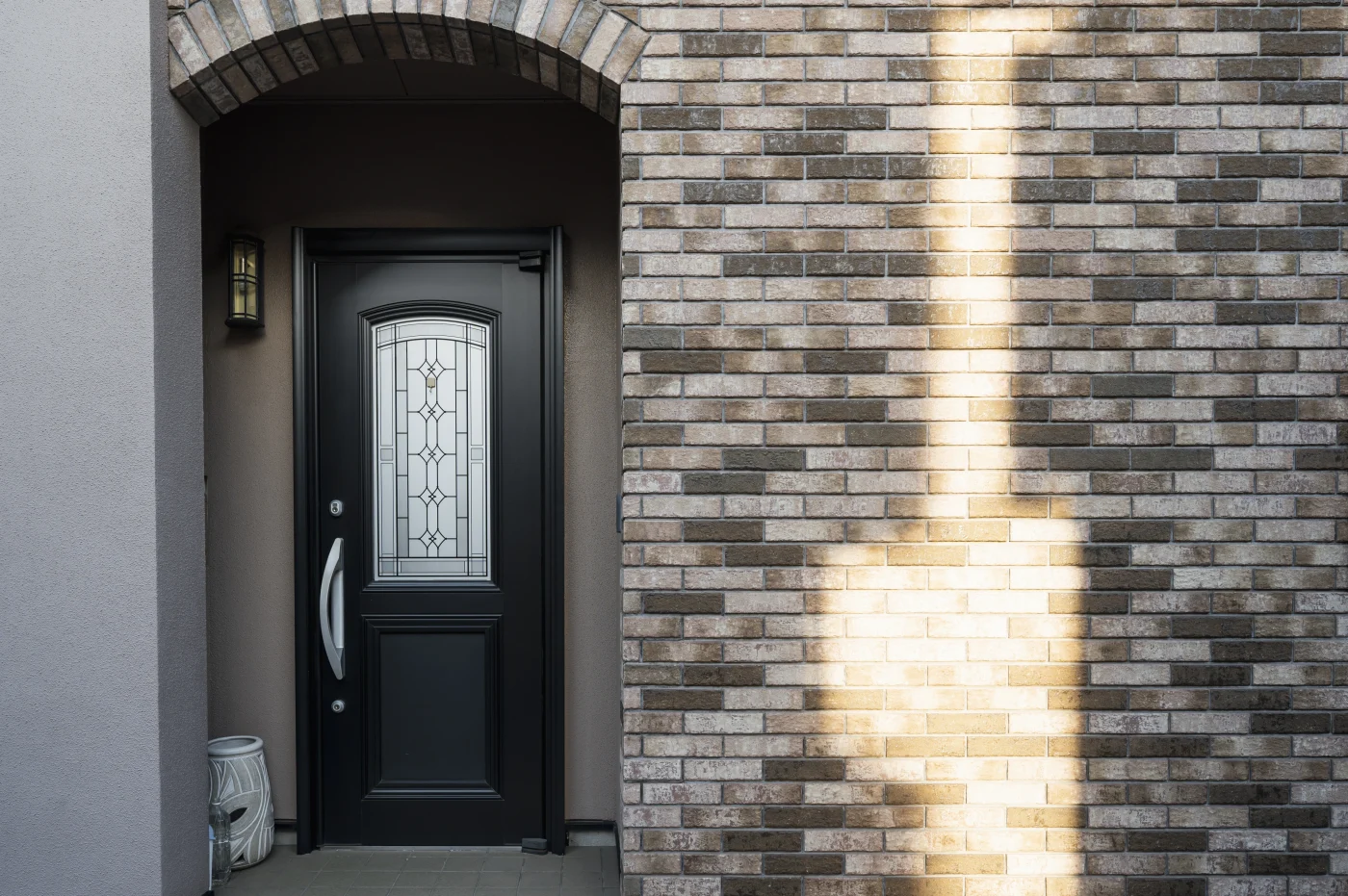 The entryway of a brown brick home. There is a black front door with a silver handle and a decorative glass window in the center.