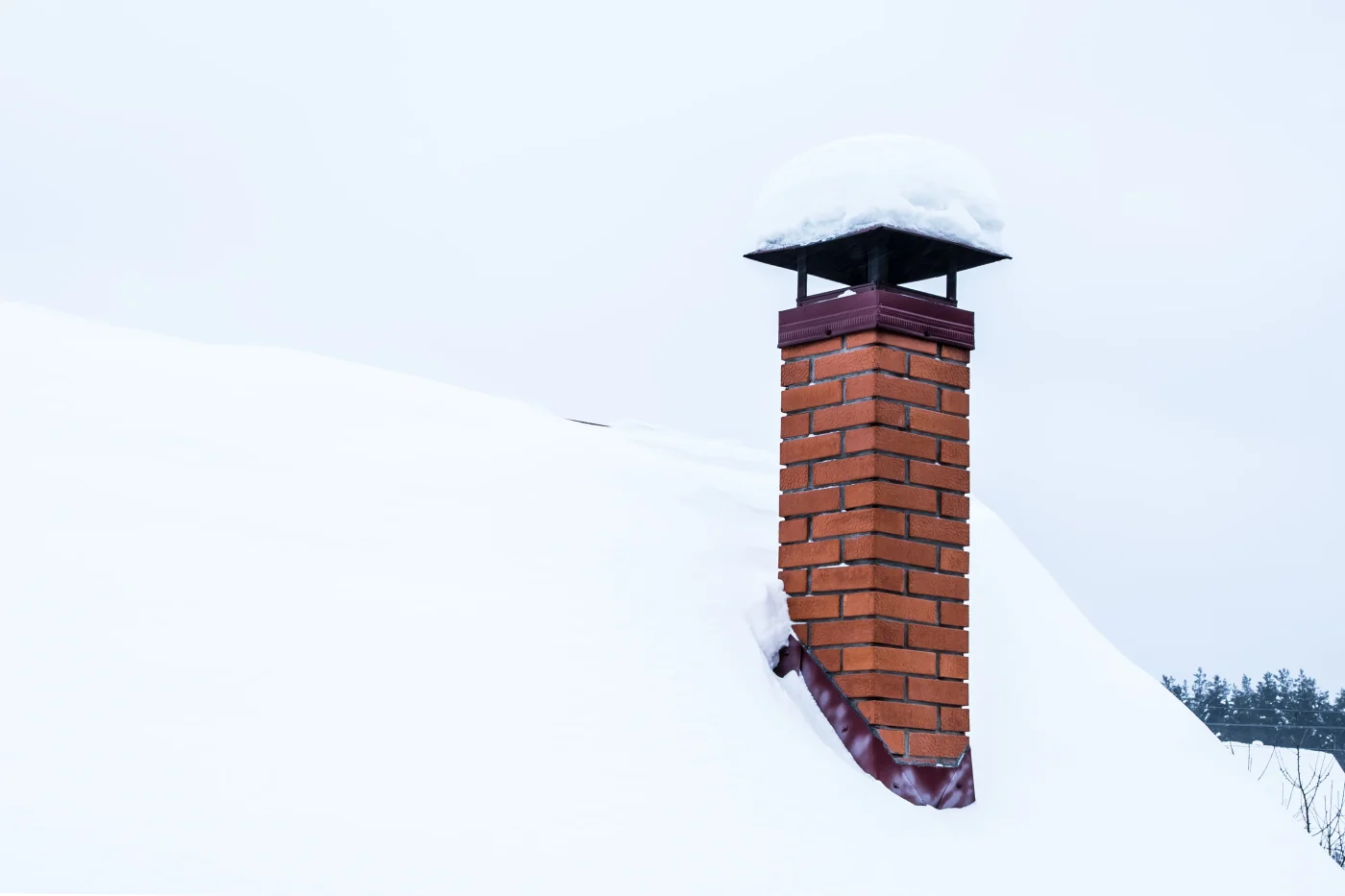 A red-brick chimney sticking up from a rooftop that is covered in snow. The crown of the chimney is a dark, purplish-brown.